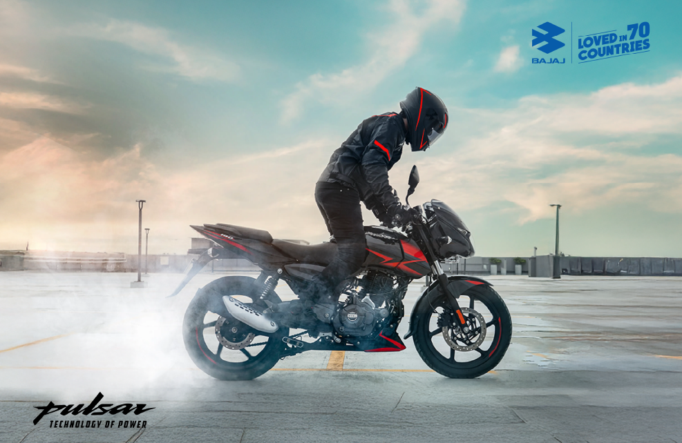 A person performing a burnout on a sleek black and red Bajaj Pulsar 150 in an open area.