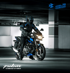 In a dark parking garage, a man is seen on a black and blue Bajaj Pulsar 150 motorcycle.